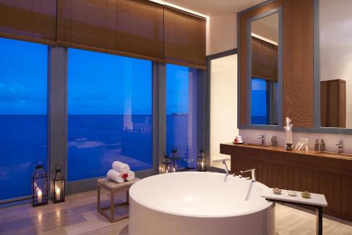 a bathroom with a large tub and large windows at Raffles Maldives Meradhoo in Gaafu Alifu Atoll