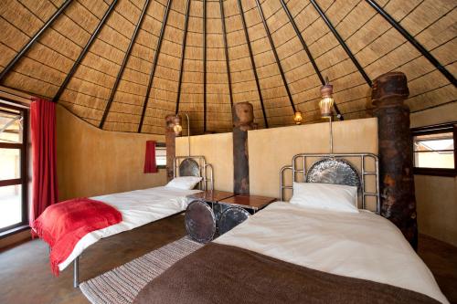 two beds in a room with a straw roof at Ongula Village Homestead Lodge in Omupumba