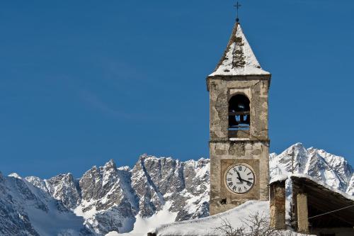 a clock tower with snow covered mountains in the background at Ca’d’ambra in Groscavallo