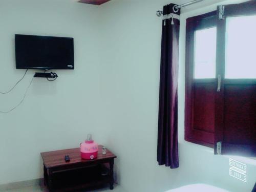 a room with a television and a table with a window at Roj Cottage in Mount Ābu