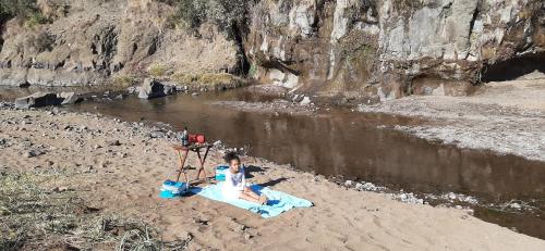 a woman sitting on a blanket in the sand next to a river at Twin Peaks Cottages and Horse Trekking in Maseru