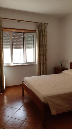 a bedroom with a bed and two windows at Alojamentos S.José in Atouguia da Baleia
