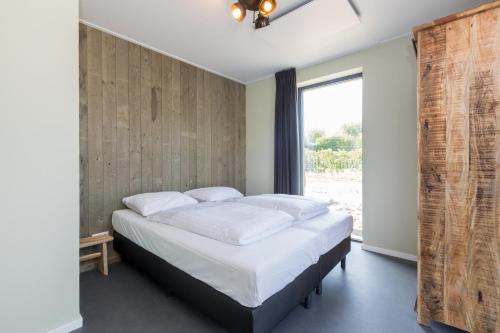 a bedroom with a bed with white sheets and a window at Welcome in - Vakantiehuis 6 en 12 personen, Vroondijk in Vrouwenpolder in Vrouwenpolder