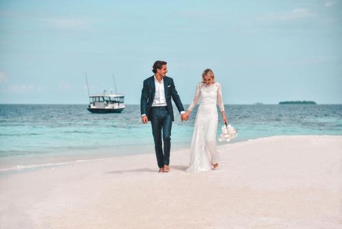 a bride and groom walking on the beach at Raffles Maldives Meradhoo in Gaafu Alifu Atoll