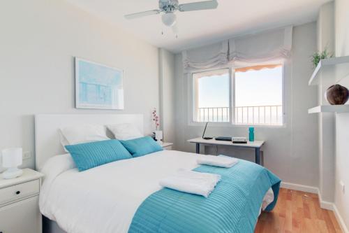 a bedroom with a large white bed with blue pillows at Apartamento Playa Victoria Cadiz in Cádiz