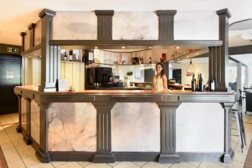 a woman standing behind a bar in a kitchen at Hôtel des Mosaiques in Orbe