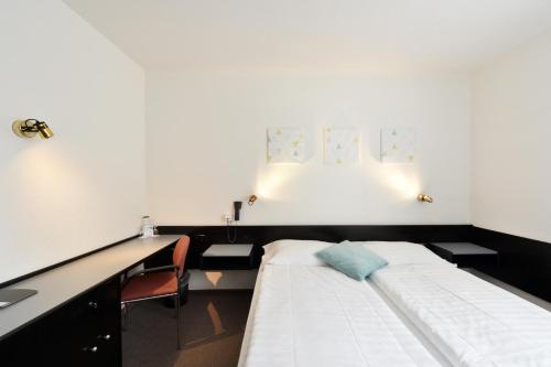 a room with a bed with a desk and a chair at Hôtel des Mosaiques in Orbe
