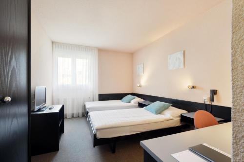 a hotel room with two beds and a television at Hôtel des Mosaiques in Orbe