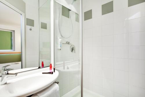 La salle de bains blanche est pourvue d'un lavabo et d'une douche. dans l'établissement ibis Budget Clermont Ferrand Centre Montferrand, à Clermont-Ferrand