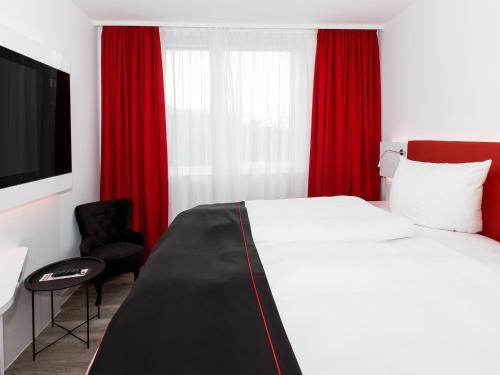 a bedroom with a bed with red curtains and a chair at DORMERO Hotel Salzgitter in Salzgitter