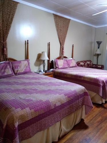 two beds in a room with purple sheets at The Great House Inn in Belize City