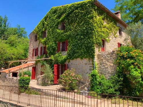 a building covered in ivy with red doors and windows at Mas Lo Faix in Saint-Laurent-de-Cerdans