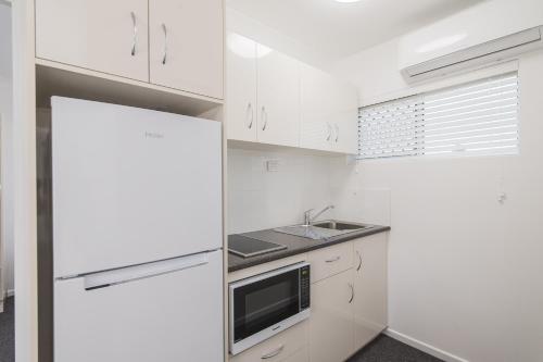 
a kitchen with white cabinets and white appliances at Metro Motel Rockhampton in Rockhampton
