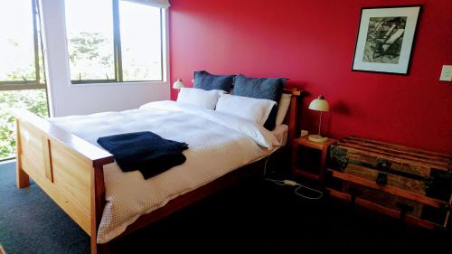 a bedroom with a large bed with a red wall at Shelly Beach Studio, Waiheke Island in Auckland