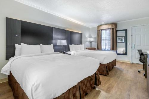 two beds in a hotel room with white sheets at Suburban Studios at the University in Conway