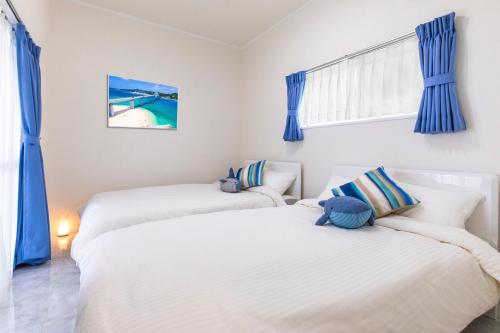 two twin beds in a room with blue curtains at Villa Piscine SESOKO -SEVEN Hotels and Resorts- in Motobu