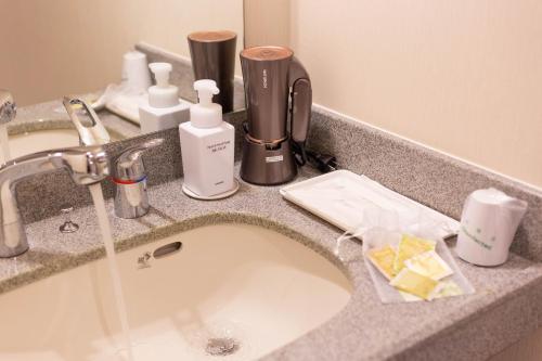 a bathroom counter with a sink with soap and cleaning products at Nami No Ue Crystal Hotel in Naha