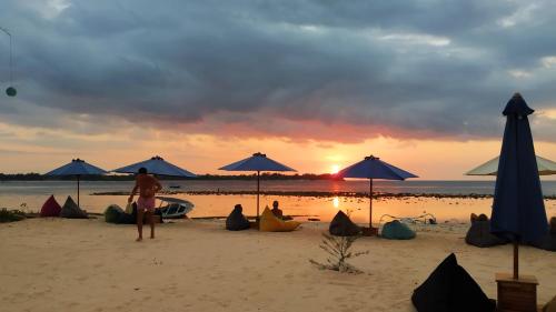 a woman standing on a beach with umbrellas at Sunset Beach Bungalow in Gili Meno