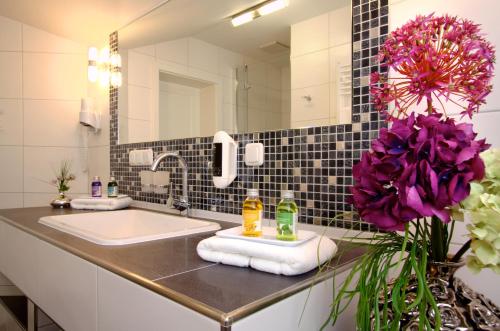 a bathroom with a sink and a mirror and purple flowers at Hotel Garni Inselparadies Zingst in Zingst