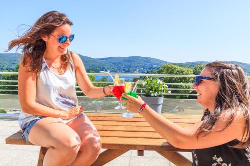 dos mujeres sentadas en un banco con bebidas en Les Fées du lac ***, en Nages