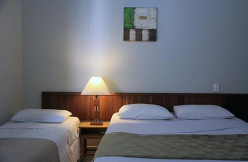 a bedroom with two beds and a lamp on a table at Castelo Palace Hotel in Batatais