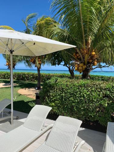 a group of chairs and an umbrella and palm trees at Cap Ouest Beachfront Luxury Penthouse & Apartment in Flic-en-Flac