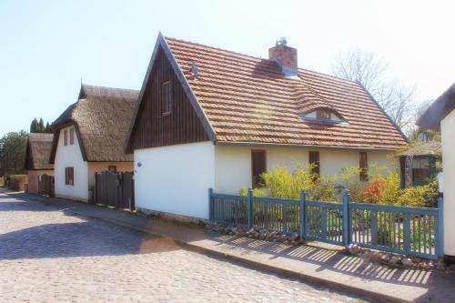 een wit huis met een zwart dak en een hek bij Haus am Wiek in Krummin