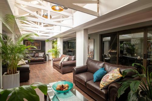 a living room with leather couches and plants at Lala Dene Lodge in Bloemfontein