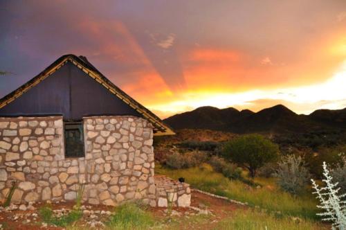a painting of a stone building with a sunset in the background at Kapika Waterfall Lodge in Epupa