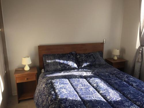 a bedroom with a bed with a blue comforter and two lamps at Condominio Robles camino al volcan in Pucón