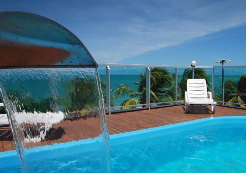a swimming pool on a balcony with a chair and the ocean at Pousada Orla dos Corais in Maragogi