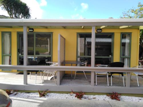 a yellow house with chairs and tables on a deck at Whatuwhiwhi TOP 10 Holiday Park in Tokerau Beach