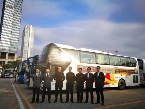 Paco Hotel Tuanyida Metro Guangzhou -Free ShuttleBus for Canton Fair في قوانغتشو: مجموعة رجال بدلاء يقفون أمام حافلة