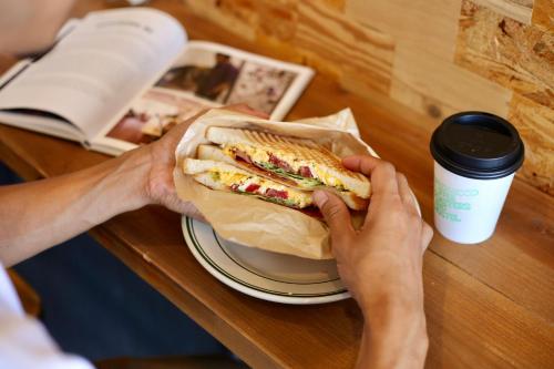 a person holding a sandwich on a table at Greenwood Hostel in Izumi-Sano