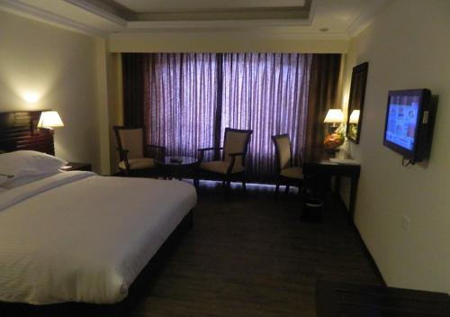 a hotel room with a bed and chairs and a television at Keshav Clarks Inn Gadag in Gadag