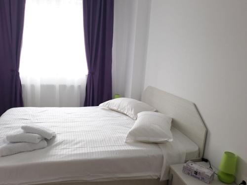 een bed met witte lakens en kussens en een raam bij Apartament Coresi in Braşov