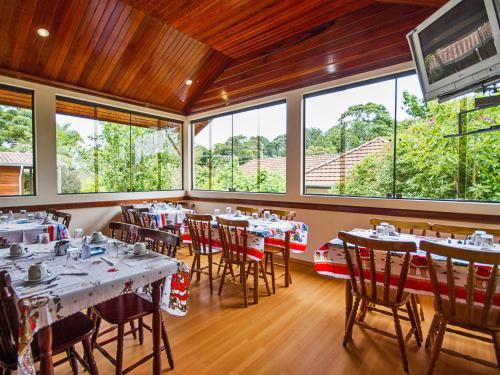 a dining room with tables and chairs and windows at Pousada Recanto São Benedito in Campos do Jordão