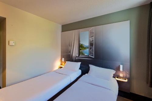 two white beds in a room with a window at B&B HOTEL Pau Zénith in Pau