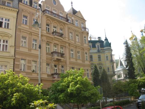 un gran edificio amarillo con árboles delante de él en Apartment Sadova en Karlovy Vary
