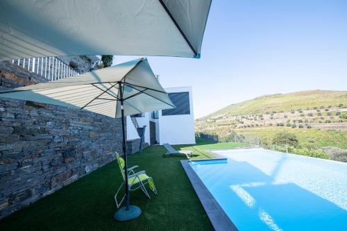 an umbrella and chairs next to a swimming pool at Casa Foz do Corgo - private pool, gardens and river access in Peso da Régua