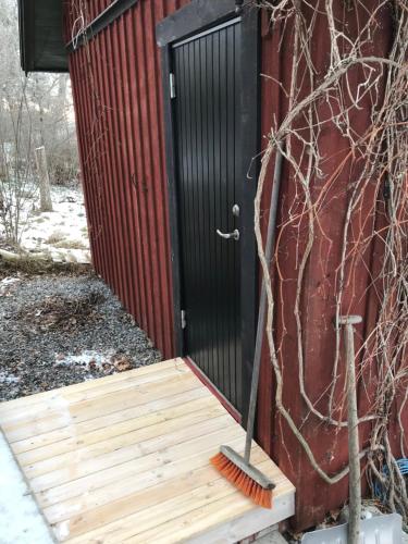 a black door on a red building with a broom at Trevlig stuga på landet, centralt 8km från Centrum in Eskilstuna