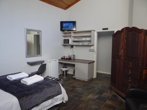a bedroom with a bed and a desk and a television at CREDO Guest House in Bloemfontein