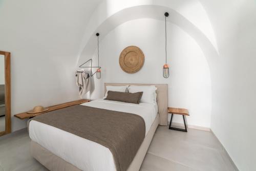 - une chambre blanche avec un grand lit et un mur dans l'établissement Echo Caves Suites, à Fira