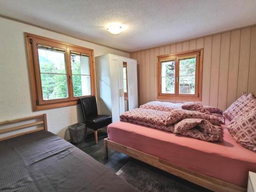 een slaapkamer met een bed en een stoel en 2 ramen bij Apartments Chalet Tatyana in Leukerbad