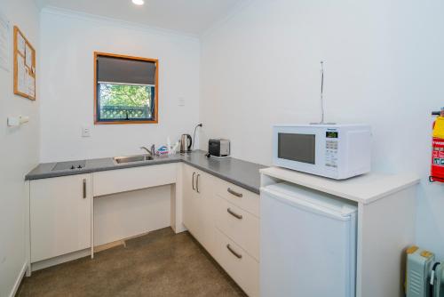 a white kitchen with a microwave and a sink at Bayside Motel Whitianga in Whitianga