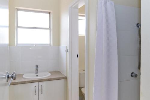 La salle de bains est pourvue d'un lavabo, d'une douche et d'une fenêtre. dans l'établissement API Pelican Beach Front Apartments Kalbarri, à Kalbarri