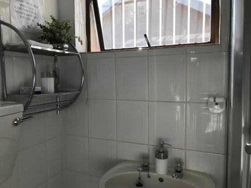 a white tiled bathroom with a sink and a window at Carrington Cottage in Cape Town