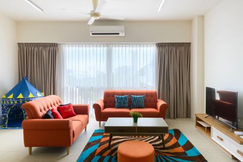 a living room with two orange chairs and a tv at By The Sea Beach Front Apartment in Batu Ferringhi