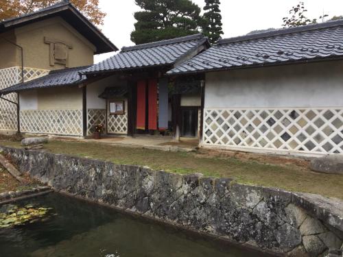 a house with a stone wall next to a pond at Guest House Shimoze Agematsu in Iida