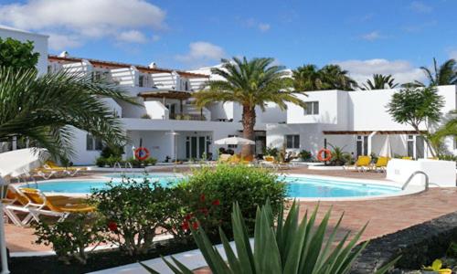 a large hotel with a swimming pool and palm trees at Apartamentos Tamarindos in Puerto del Carmen